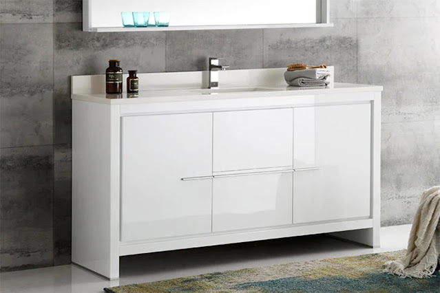 Modern white vanity with single sink and silver faucet against a gray tiled wall with rug in front.