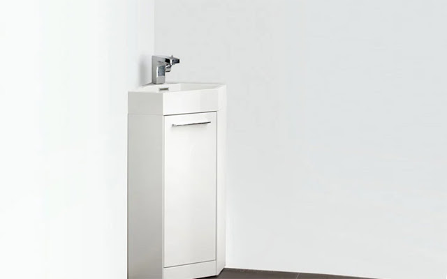 Small white vanity with sink and silver faucet in the corner of a small white bathroom.